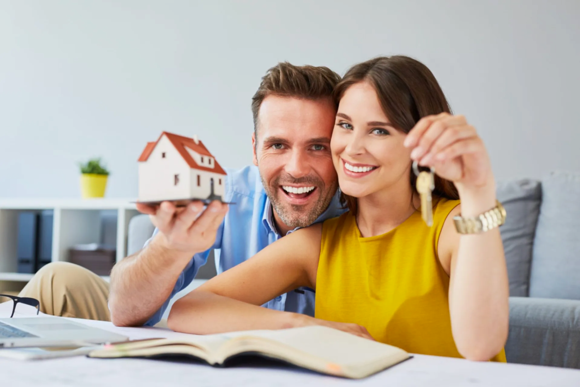 A couple looking at the camera, holding a miniature house and a pair of keys.